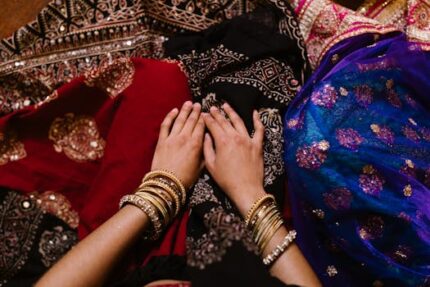 Top view of hands adorned with bangles resting on vibrant traditional fabrics, showcasing cultural fashion.